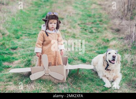 bambino nei vestiti dell'aviatore ed il suo co-pilota vicino all'aereo del cartone Foto Stock