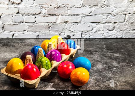 Cartoncino con uova di pasqua colorate di fronte al muro di mattoni bianchi Foto Stock
