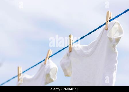 Abiti bianchi appesi sulla corda all'aperto contro il cielo blu Foto Stock