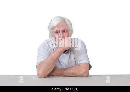 Scatto orizzontale di un vecchio seduto a un tavolo con la mano al mento nel profondo del pensiero. Isolato su bianco. Molto spazio di copia. Foto Stock