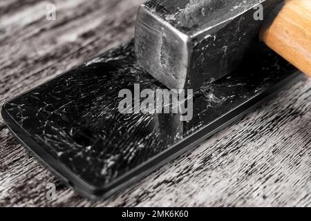 Smartphone con un display rotto e un martello. Rottura del touchscreen schiacciato di un dispositivo elettronico Foto Stock