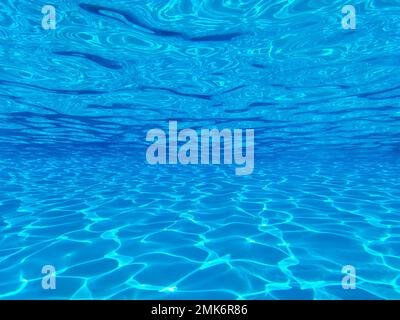 La vista attraverso un porto panoramico tra il pavimento, il fondo e la superficie della lussuosa piscina e l'acqua blu con riflessi del sole presso il resort Foto Stock