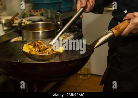 Le mani di uno chef asiatico mescolano friggere un wok manzo con bambù nella cucina di un ristorante europeo cinese Foto Stock