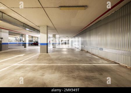 Garage di un edificio residenziale con spazi delimitati da vernice bianca e pareti ricoperte da lastre metalliche Foto Stock