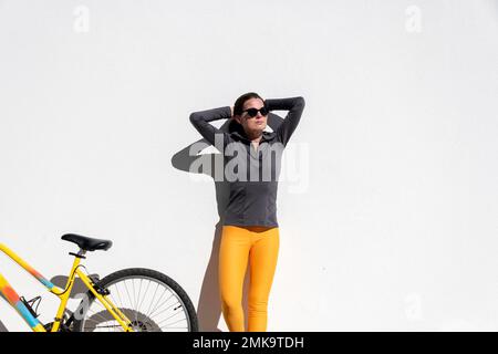 donna in piedi contro un muro con la sua bicicletta al sole Foto Stock