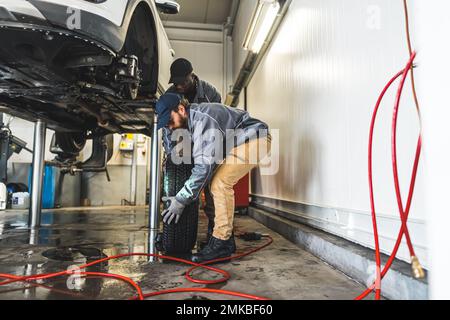 I meccanici dell'automobile sono occupati sostituire le ruote di un'automobile sull'ascensore in un negozio di riparazione auto. Foto di alta qualità Foto Stock