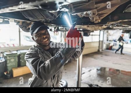 Un meccanico che sostituisce la frizione di un'auto sollevata utilizzando una torcia in un'officina di riparazione auto. Foto di alta qualità Foto Stock