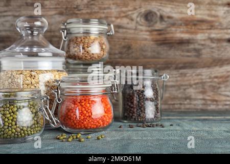 Diversi tipi di legumi e cereali in vasetti di vetro su tavola di legno blu, spazio per il testo. Grani organici Foto Stock