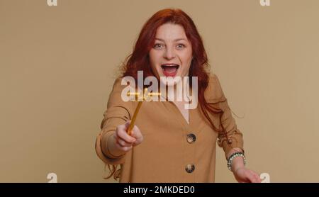 Strega mago donna gesturing con bacchetta magica bastone fata, rendendo il desiderio diventare realtà, casting magia mago, pubblicità vacanze vendita sconto. Giovane ragazza rossa isolata su sfondo beige studio Foto Stock