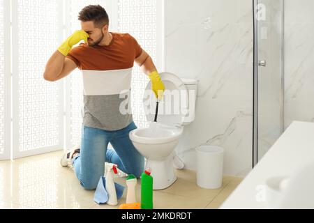 Giovane uomo che sente disgusto mentre pulisce il water ciotola in bagno Foto Stock