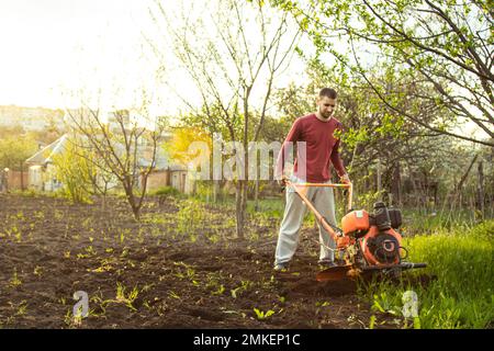 Un agricoltore lavora sul campo, arando il terreno con un aratro sull'azienda. Un arciatore su una passeggiata dietro un motocoltivatore. Stagione di dissodamento. Culto biologico Foto Stock