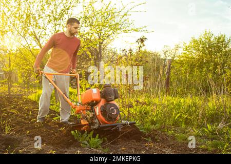 Un agricoltore lavora sul campo, arando il terreno con un aratro sull'azienda. Un arciatore su una passeggiata dietro un motocoltivatore. Stagione di dissodamento. Culto biologico Foto Stock