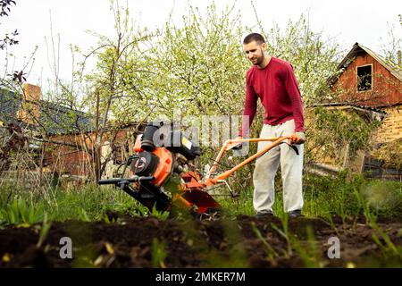 Piantando vegetali sotto il trattore di walk-behind. Un uomo con un trattore in giardino. Lavoro manuale con l'attrezzatura. Un uomo anziano insegna Foto Stock