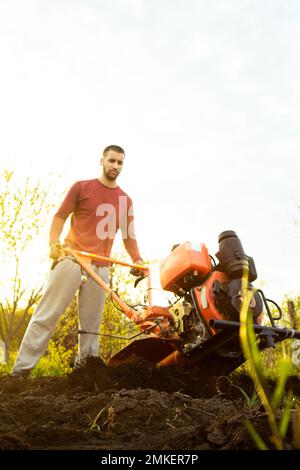 Un agricoltore lavora sul campo, arando il terreno con un aratro sull'azienda. Un arciatore su una passeggiata dietro un motocoltivatore. Stagione di dissodamento. Culto biologico Foto Stock