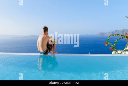 Uomini che si rilassano in una piscina infinity durante le vacanze a Santorini, piscina che si affaccia sul mare Caldera di Santorini, Oia Grecia, Grecia isola greca Cicladi vacanza di lusso. Foto Stock