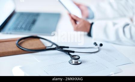 Stetoscopio, scrivania e documenti con mani, tablet o ricerca per medico in ospedale. Area di lavoro clinica sanitaria, comunicazione telemedicina o. Foto Stock