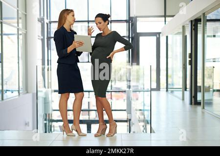 Due menti sono meglio di una. Immagine a tutta lunghezza di due giovani donne d'affari in piedi insieme in un ufficio moderno e lavorando su un tablet. Foto Stock