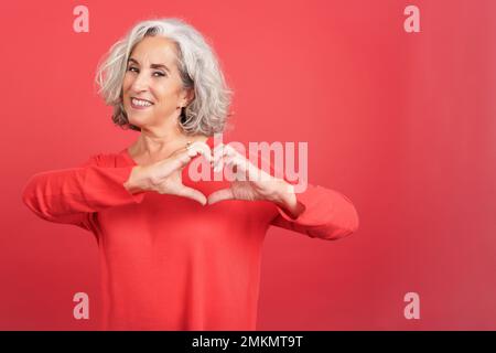 Donna matura che rappresenta un cuore a forma di dita Foto Stock