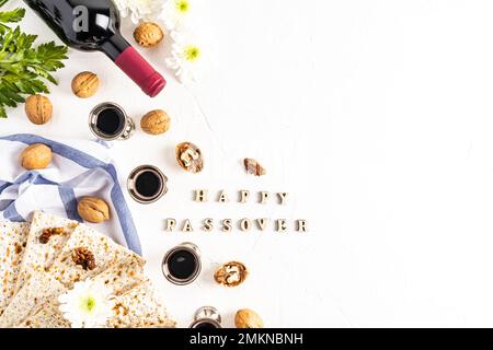 Sfondo festivo della Pasqua ebraica con matzah, vino rosso kosher e bicchieri d'argento, noci su sfondo bianco con il testo Happy Passover Foto Stock