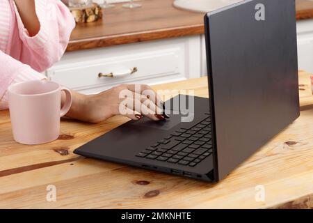 donna in accappatoio dopo una doccia mangia delizioso dessert per la prima colazione in casa ufficio. donna di mezza età lavora a casa al computer in cucina. Foto Stock