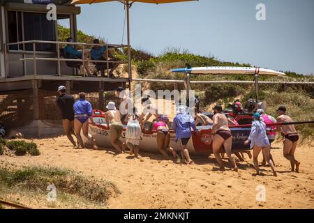 Sydney Northern Beaches Surfboat carnevale a North Narrabeen Beach, gli equipaggi di Surfboat rimuovono il Surfboat dalla spiaggia utilizzando i parafanghi per barche a rolling boat Foto Stock