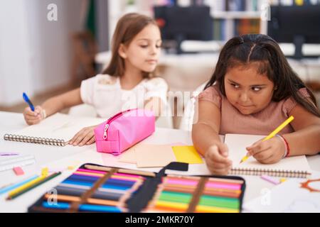 Due studenti bambini seduti sul tavolo disegnando su un foglio di carta in classe Foto Stock