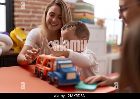 Insegnanti con ragazzo e ragazza che giocano con auto giocattolo seduto sul tavolo all'asilo Foto Stock