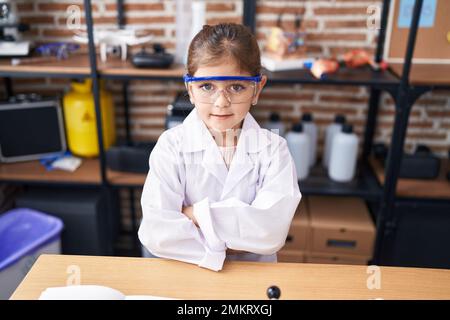 Adorabile ragazza ispanica studente scienziato sorridente fiducioso in piedi con braccia incrociate gesto in classe laboratorio Foto Stock