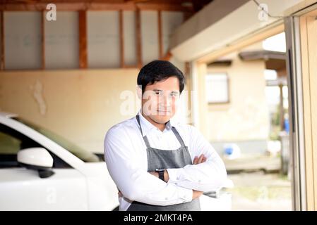 Un uomo che indossa un grembiule al braccio trasversale del garage Foto Stock