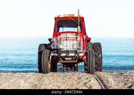 Un vecchio trattore MF 135 Massey-Ferguson rosso è dotato di un rimorchio per imbarcazioni vuoto sulla spiaggia sabbiosa sulla riva di Kattegatt, Djursland, Jutland, Danimarca Foto Stock