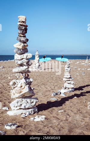 Due surfisti camminano oltre la pietra di selce cairns sulla spiaggia sabbiosa di Klitmöller, costa occidentale dello Jutland, Danimarca Foto Stock