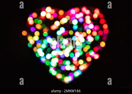 Cerchi di luce multicolore con effetto bokeh a forma di cuore su sfondo nero (sfondo per San Valentino) Foto Stock