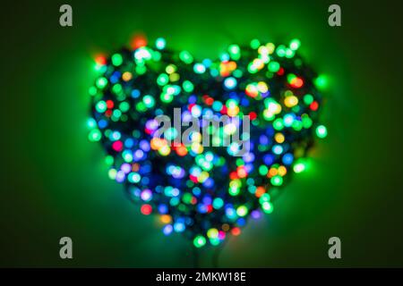 Ghirlanda sfocata con luci multicolore piegate a forma di cuore su sfondo verde scuro Foto Stock