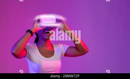 Excited Young African American Woman indossa occhiali VR luminosi in Neon Light Foto Stock