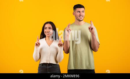 Giovane ragazza e ragazzo orabico e allegro pensivo in casual con le dita incrociate, pensando, sognando Foto Stock