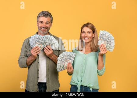 Grande fortuna e vincere concetto. Sposi di mezza età eccitati che detengono un sacco di dollari in contanti, celebrando il successo insieme Foto Stock