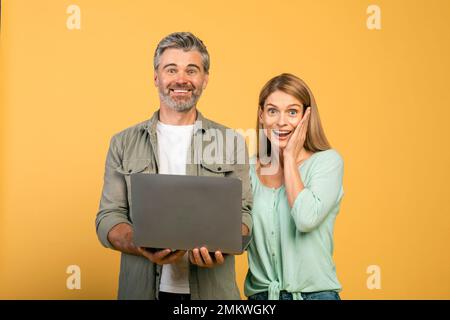 Offerta incredibile, buone vendite. Sorpresi gli sposi caucasici di mezza età che tengono il laptop e guardano la fotocamera con la bocca aperta Foto Stock