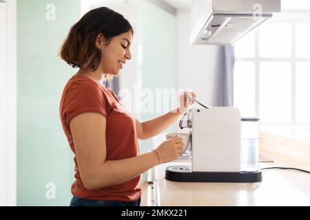 Giovane donna araba sorridente che prepara caffè fresco con moderna macchina in cucina Foto Stock