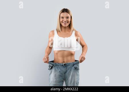 Felice giovane donna che indossa jeans grandi dopo la perdita di peso su sfondo turchese Foto Stock
