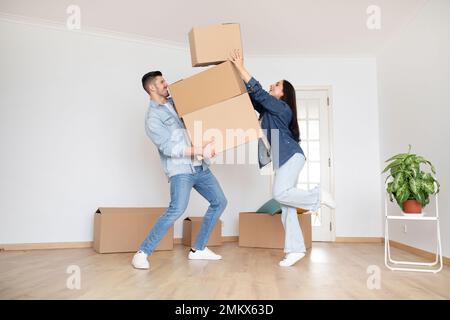 Giorno del trasferimento. Sposi giovani felici che trasportano le scatole di cartone mentre si muovono, Foto Stock
