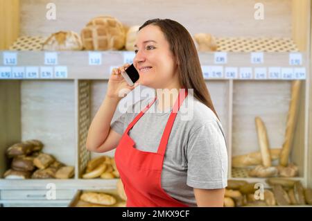 donna commerciale con grembiule che utilizza uno smartphone presso il panificio Foto Stock