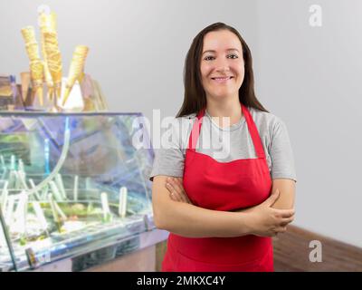 Un dipendente sorridente del negozio di gelati in piedi dietro il bancone del negozio con le braccia incrociate Foto Stock