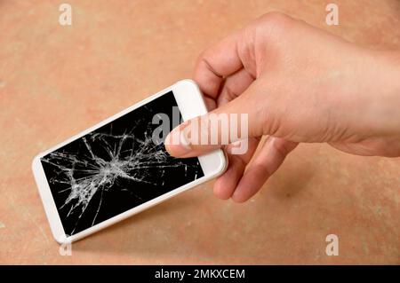 Persona che picking smartphone rotto con schermo rotto sul pavimento a casa Foto Stock