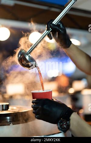 versare il cucchiaio in un bicchiere di vin brulé caldo Foto Stock