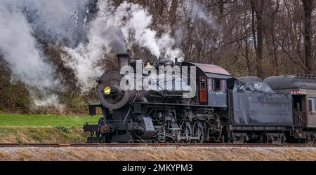 Una vista di un treno passeggeri a vapore classico, che soffia molto fumo e vapore, mentre si viaggia in campagna in un giorno d'autunno Foto Stock