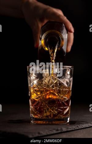 Il barista versa il whisky o il rum in un bicchiere, primo piano Foto Stock