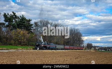 Vedi os un classico treno a vapore passeggeri che passa lentamente passato campi di mais raccolti in un giorno d'autunno Foto Stock
