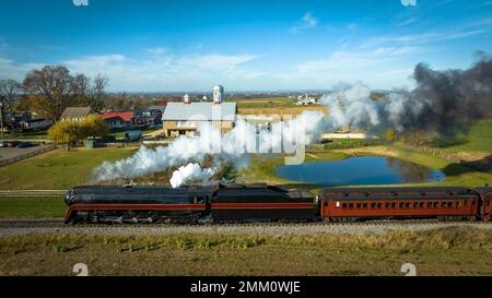 Veduta aerea parallela di un treno a vapore antico restaurato che viaggia attraverso la campagna in un giorno d'autunno soleggiato Foto Stock