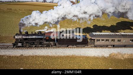 Veduta aerea parallela di un treno a vapore antico restaurato che viaggia attraverso la campagna in un giorno d'autunno soleggiato Foto Stock