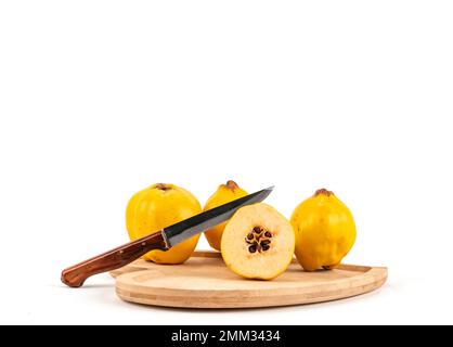 Sul tagliere di legno appaiono le cotogne tagliate con un coltello da semi a metà. Semi di cotogna con coltello sul tagliere piatto di legno fondo bianco. Foto Stock